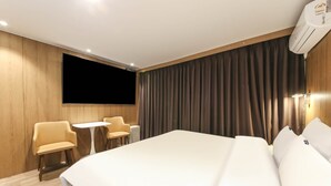 Habitación de hotel con una cama grande, un televisor de pantalla plana montado en la pared, una mesita con dos sillas y una ventana con cortinas.
