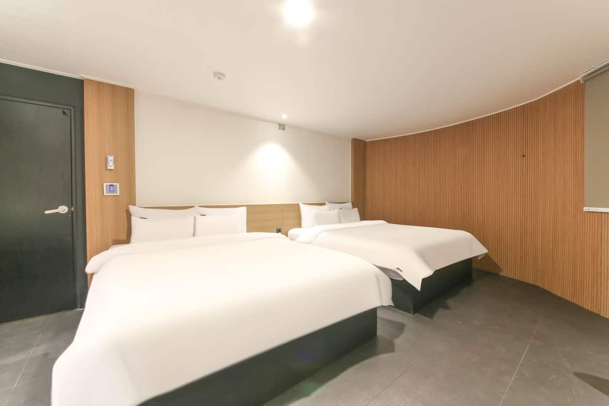 A hotel room with two beds, a wooden panel wall, a dark door, and a light-colored floor.