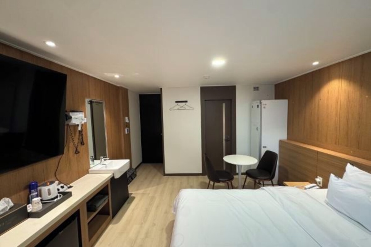 A hotel room with a bed, a desk with a TV, a mirror, a small table with chairs, and a wardrobe.