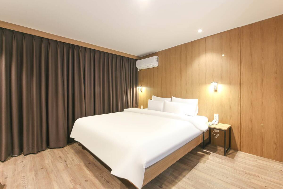 A modern hotel room with a large bed, wooden panel walls, and a wooden floor.