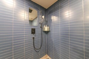 Une salle de bain avec des murs recouverts de carreaux bleus, une douche avec un pommeau de douche amovible et une étagère contenant des articles de toilette.