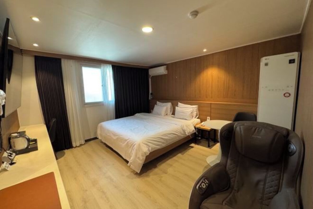 A hotel room with a bed, bedside table, chair, and a TV.