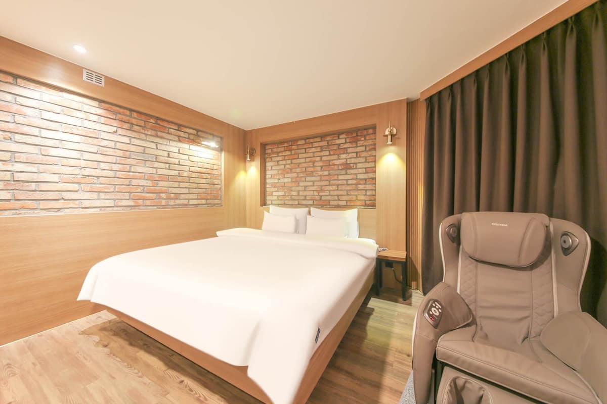 A hotel room with a large bed, a wheelchair, and a brick wall.