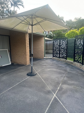 Relax under the covered patio, shaded by a retractable awning and surrounded by lush greenery.