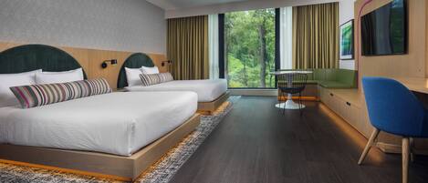 A modern hotel room with two beds, a desk, a chair, and a large window offering a view of greenery.