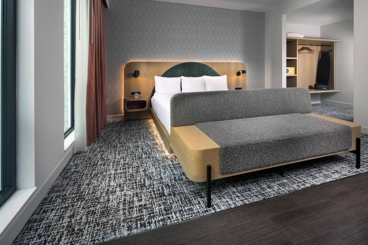 Ein modernes Hotelzimmer mit Bett, Nachttisch, eingebautem Kleiderschrank und großem Fenster.