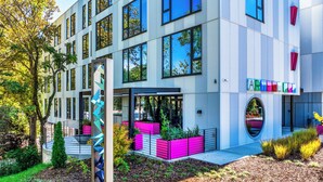 Un bâtiment moderne doté de nombreuses fenêtres, d’une sculpture centrale et de jardinières colorées.