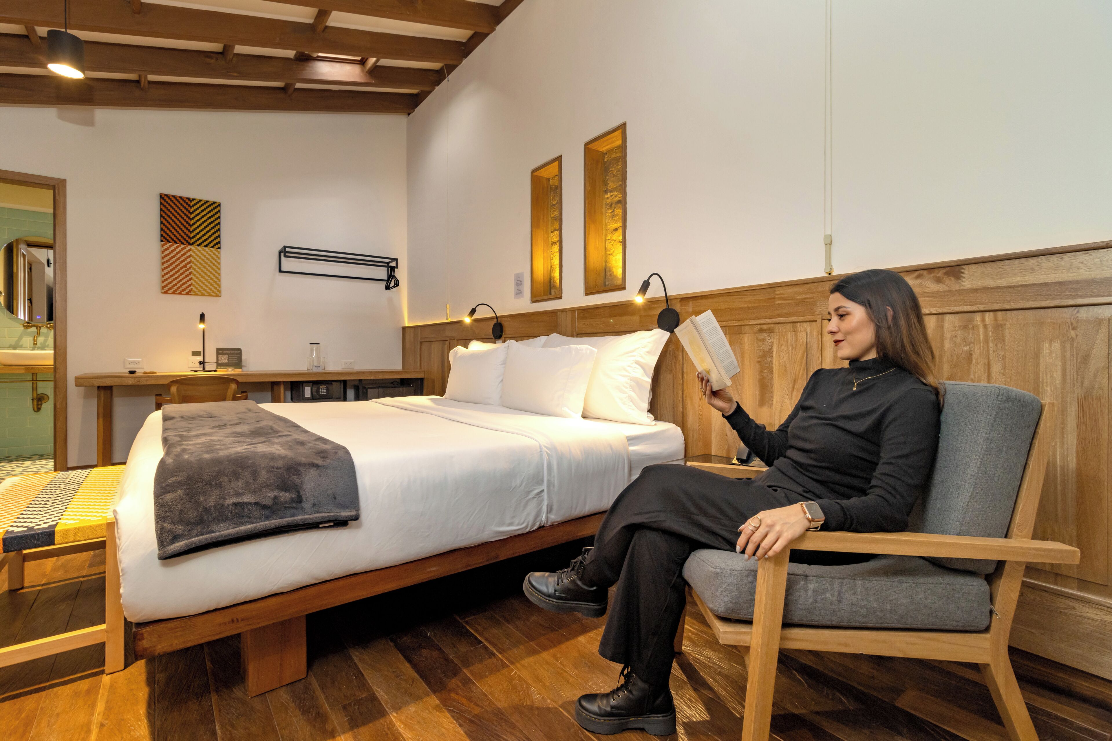 Une chambre à coucher moderne avec un lit en bois, une table de chevet, une chaise et une lampe fixée au mur.