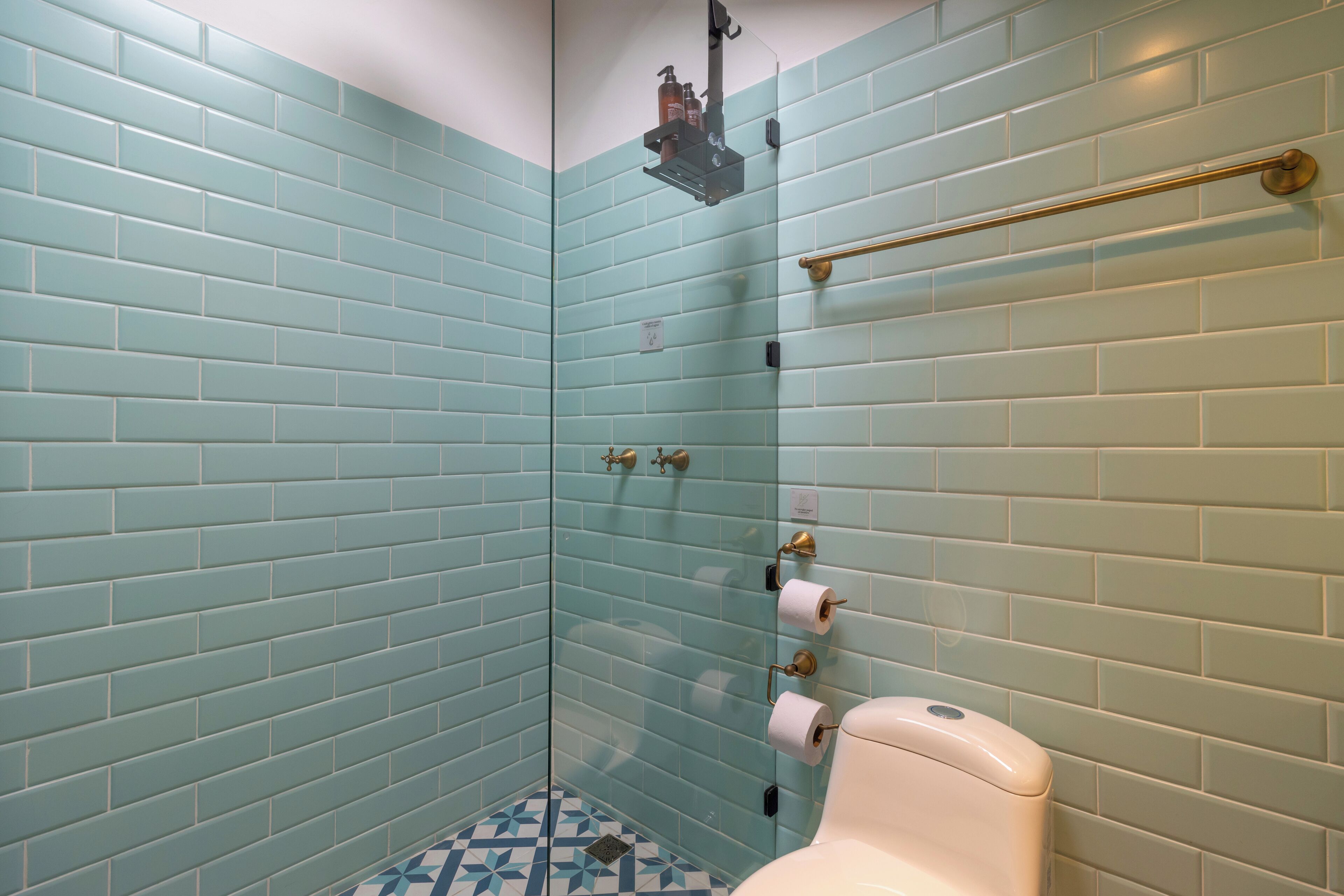 A bathroom with teal tiles, a toilet, and a shower area.