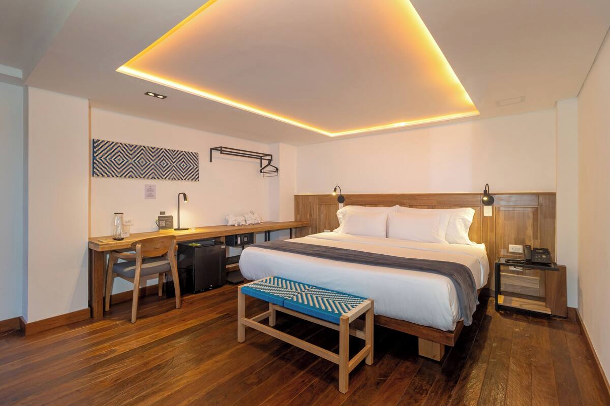 A modern hotel room with a wooden bed, a desk, and a bench.
