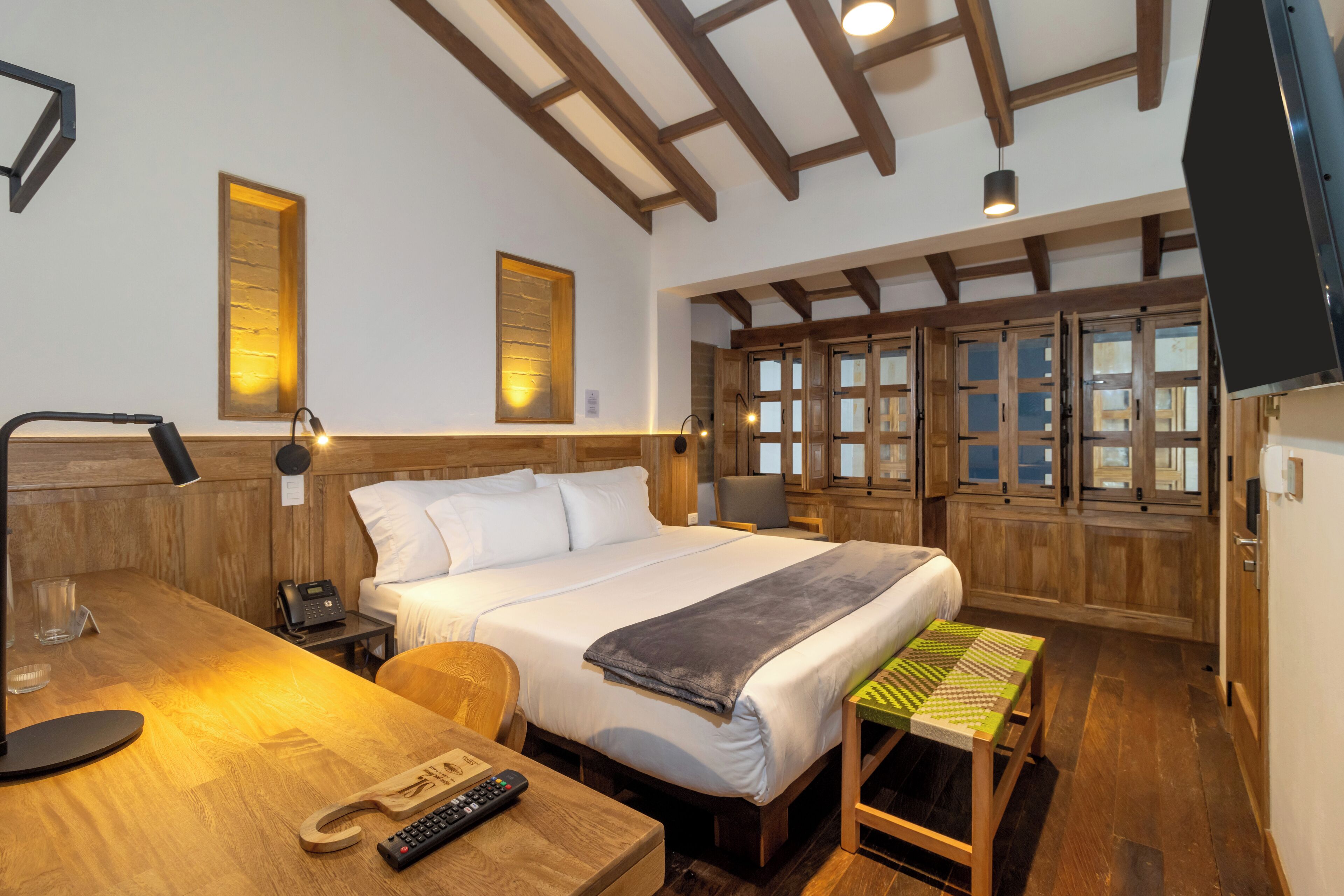 A hotel room with a wooden bed, a desk with a lamp, a telephone, and a television.