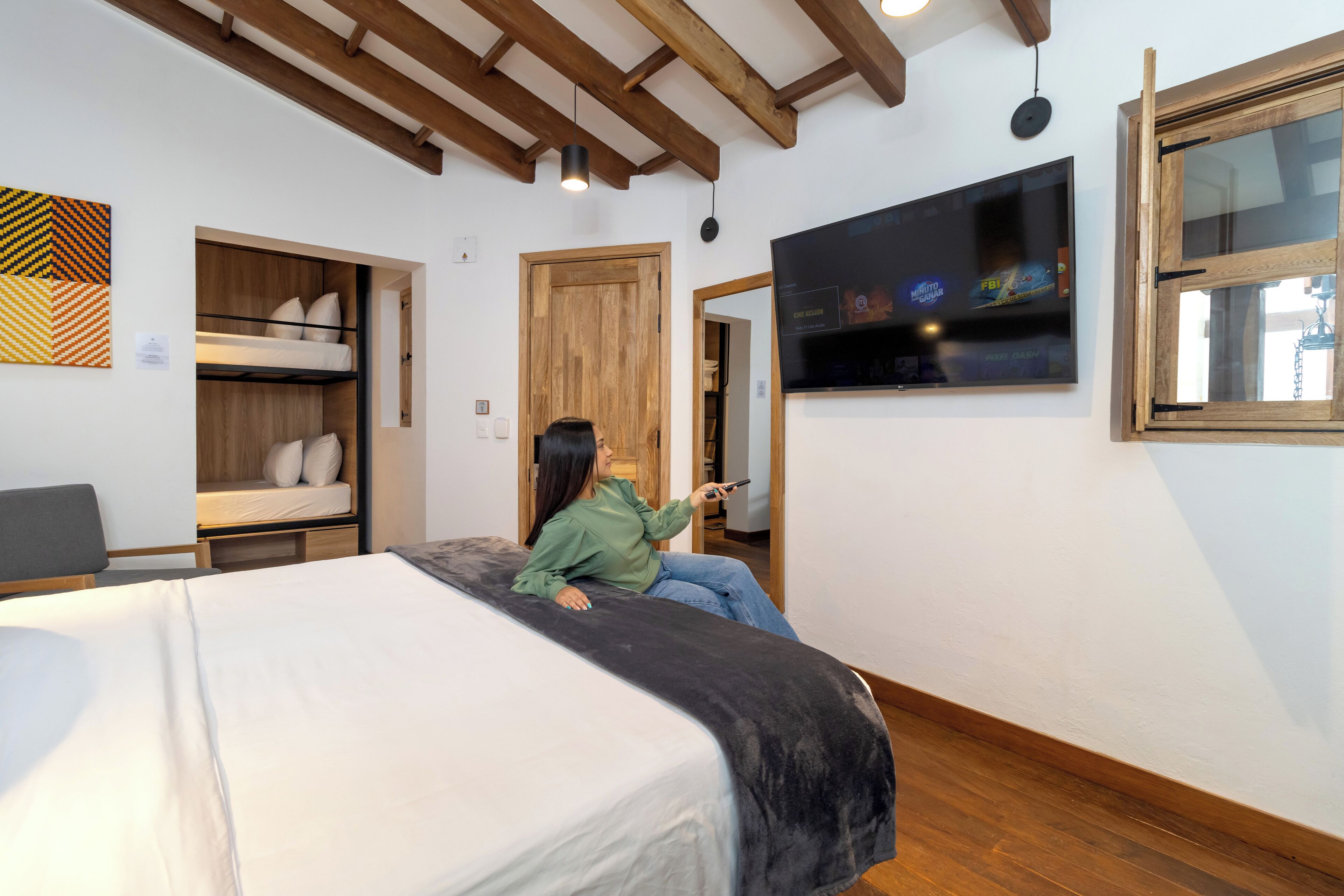 A room with a bed, a bunk bed, a TV, and a wooden ceiling.