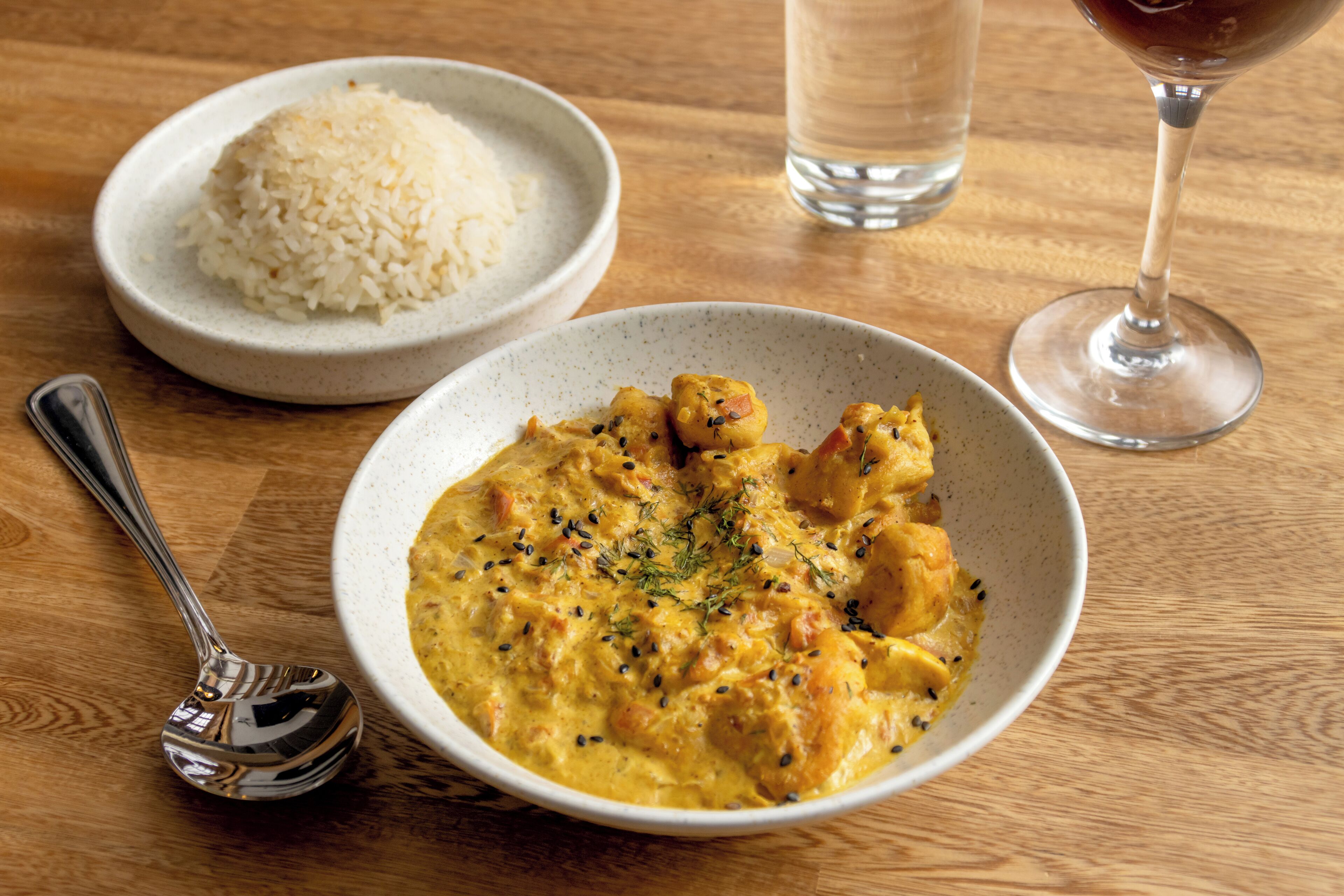 A table with a bowl of curry, a bowl of rice, a glass of water, and a wine glass.