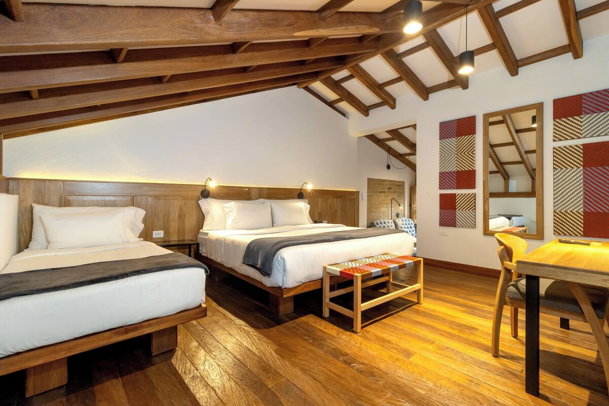 A room with two beds, wooden flooring, and a dining table.