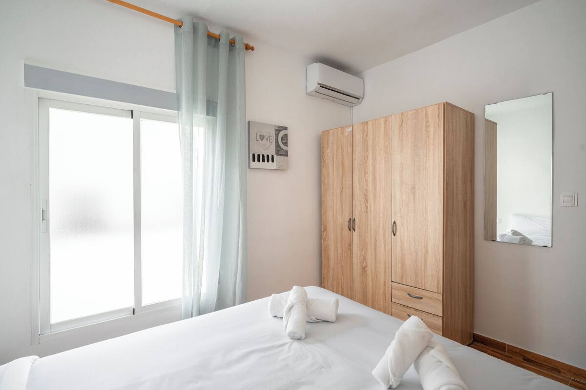 Une chambre d’hôtel avec un lit, une armoire en bois, une fenêtre avec des rideaux et un appareil de climatisation.