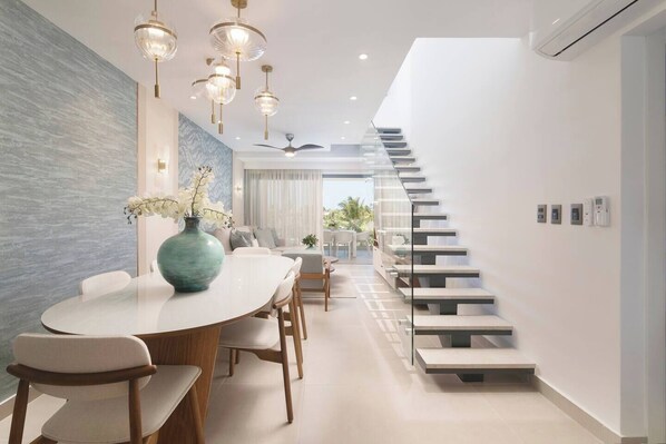 A modern interior with a dining area, a staircase, and a view to the outdoors.