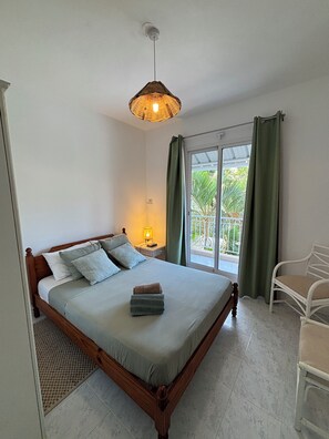 Una cama bien hecha con almohadas, una lámpara de noche, una silla y vistas al verdor por una ventana.