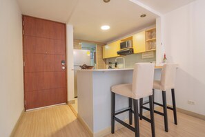 Cozinha compacta com porta de madeira, micro-ondas e dois bancos altos.
