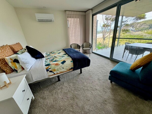 Habitación de hotel con cama, escritorio, sillón y sofá, y un ventanal con vistas al exterior.