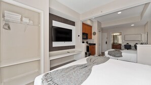 Une chambre d’hôtel moderne dotée d’un grand lit, d’un téléviseur fixé au mur, d’une kitchenette et d’un dressing.