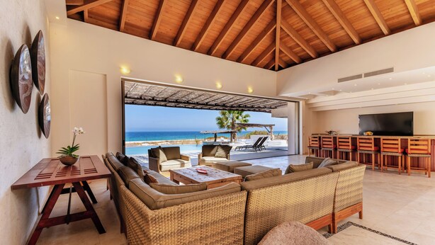Amplia sala de estar con un ventanal grande con vistas a la playa, un conjunto de asientos cómodo y una zona de bar.
