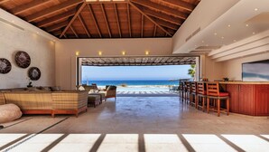 Amplia sala de estar con vista a la playa, techo de madera y zona de bar.