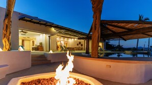 Un área de piscina moderna al aire libre con una chimenea, un patio cubierto y vistas del interior.