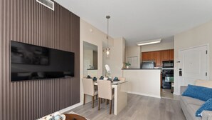 A modern living room with a flat-screen TV, a dining area with a table and chairs, and a kitchen in the background. - King Bed Suite, Kitchen, Near Theme Parks (Orlando)