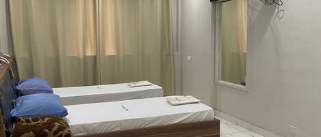 A hotel room with two beds, a wooden headboard, a flat-screen TV mounted on the wall, and a window with curtains.