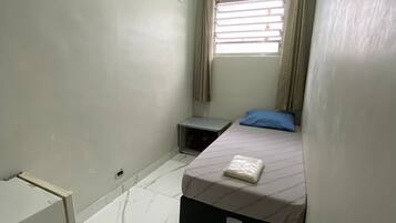 A small, well-lit bedroom with a single bed, a nightstand, a window with curtains, and a ceiling light.