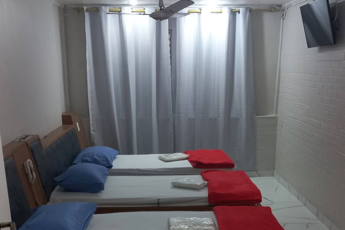 Hotellihuoneessa on neljä sänkyä, ja jokaisessa on tyyny ja peitto. Huoneessa on lisäksi kattotuuletin, seinälle asennettu televisio ja ikkuna, jossa on verhot.