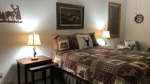 Ein Schlafzimmer mit einem Bett, zwei Nachttischen, einer Lampe, einem gerahmten Bild an der Wand und einer Uhr.