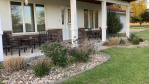 Eine überdachte Terrasse mit Sitzgelegenheiten, eine Ziegel-Fassade und ein angelegter Gartenbereich.