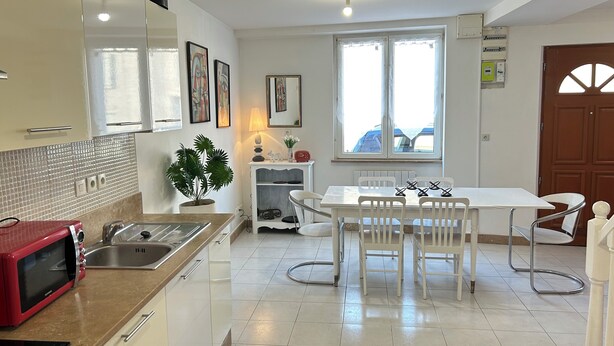 Une cuisine moderne avec des meubles blancs, un micro-ondes rouge et un coin repas comprenant une table et des chaises blanches.