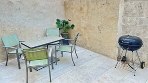 Une terrasse extérieure avec une table et des chaises, un pot de fleurs et un barbecue.