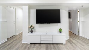 Een moderne woonkamer met een flatscreen televisie aan een witte tv-meubel, twee potplanten en een houten vloer.