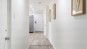 Een hal met een witte deur aan het einde, een koelkast en kunstwerken in een lijst aan de muur.