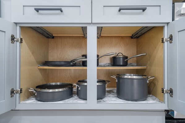 A kitchen cabinet with four pots and pans, two shelves, and a marble countertop.