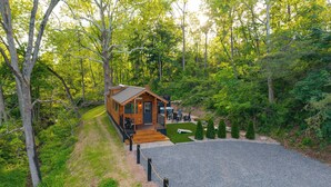 Une cabane en bois dotée d’une terrasse et d’un espace salon extérieur, le tout entouré d’une forêt dense.
