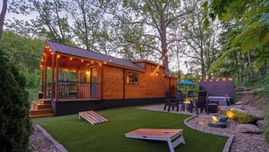 Une cabane en bois dotée d’une véranda, d’un espace extérieur aménagé pour s’asseoir et d’un foyer.