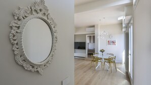 Ein modernes Interieur mit einem weißen, verzierten Spiegel, einem Essbereich mit gelben Stühlen und einer Küche im Hintergrund.