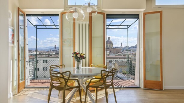 Ein Essbereich mit Tisch und Stühlen, einer Blumenvase und großen Fenstern mit Blick auf die Stadt.