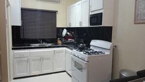 A kitchen with white cabinets, a black countertop, a stove, and a microwave. - 3-bedroom in lovely Amity Hall with WiFi, AC, Private Bathrooms, Best View (Amity Hal)