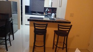 A compact kitchen with a black countertop, two wooden bar stools, and a refrigerator. - 3-bedroom in lovely Amity Hall with WiFi, AC, Private Bathrooms, Best View (Amity Hal)
