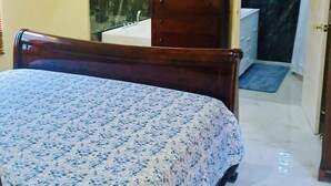 A bedroom with a bed, a TV mounted on the wall, a bathroom with a mirror, and a door leading to another room. - 3-bedroom in lovely Amity Hall with WiFi, AC, Private Bathrooms, Best View (Amity Hal)