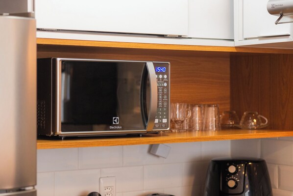 A microwave oven with a digital display and control panel, placed on a wooden shelf in a kitchen. - SUH Copacabana 43 New Comfort (Rio de Janeiro)