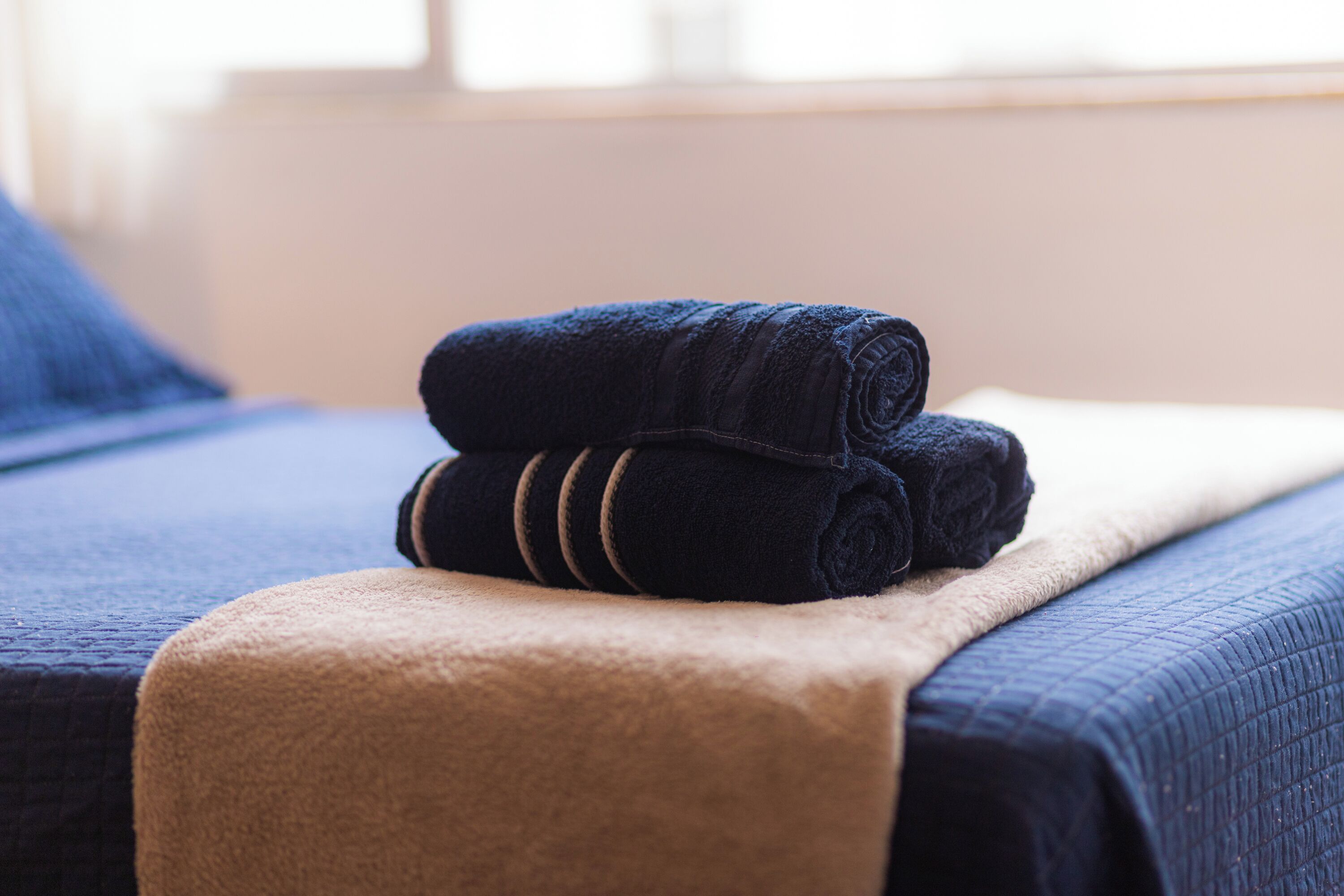 A neatly made bed with a dark blue blanket and a beige throw.