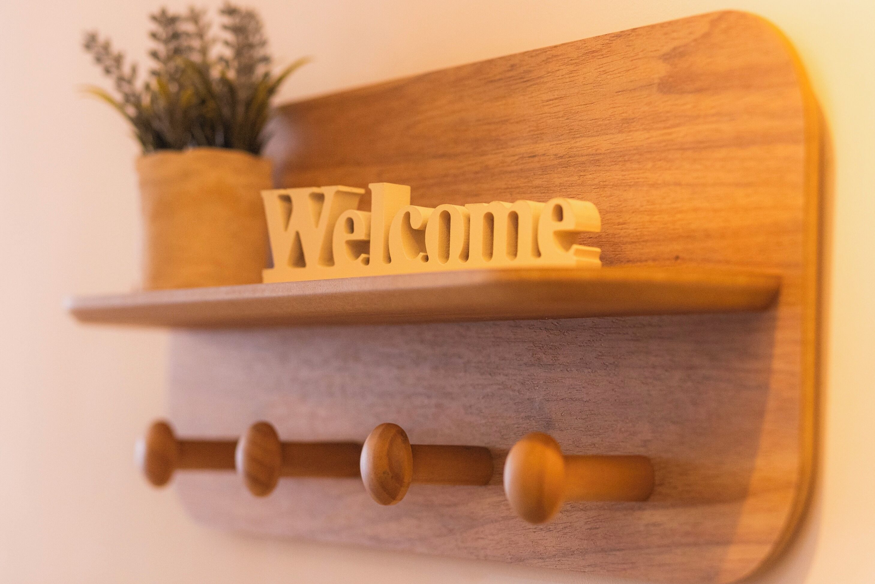 Un estante de madera fijado a la pared con la palabra “Welcome” y una pequeña planta en maceta.