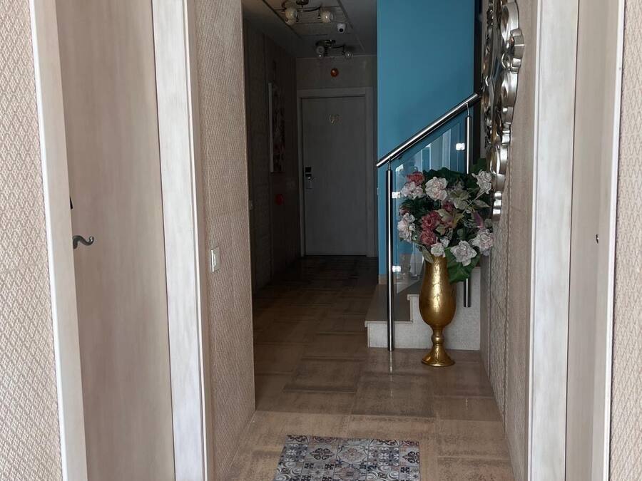 Um corredor com um tapete estampado, uma escada com guarda-corpo de metal e um vaso decorativo com flores.