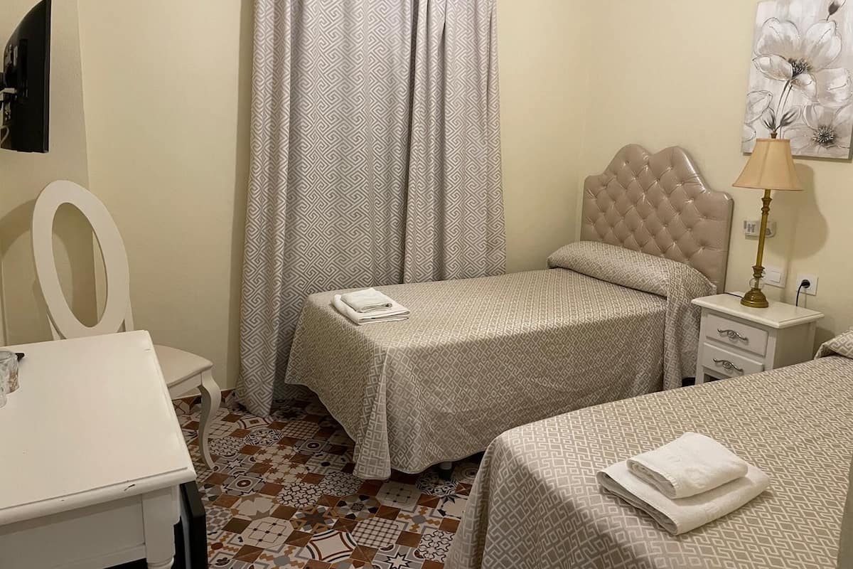 A bedroom with two beds, a desk, a chair, a lamp, and a painting on the wall.